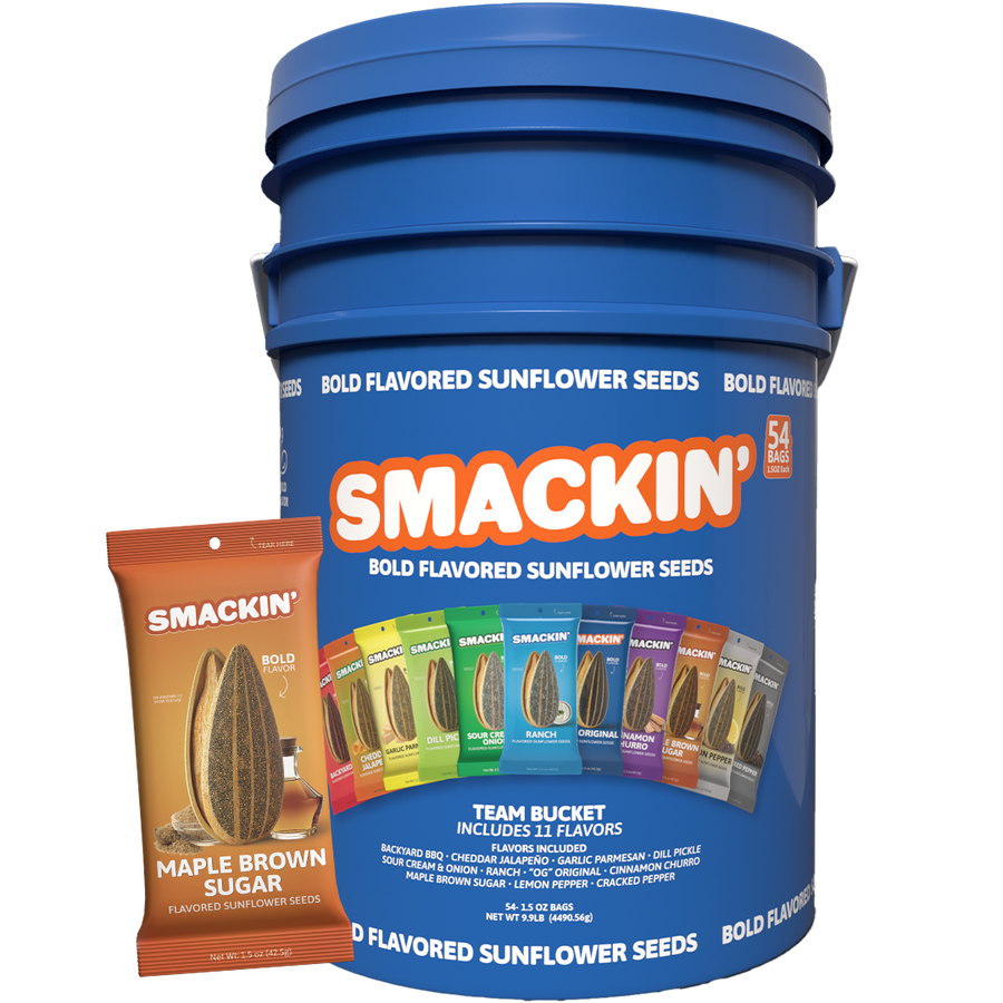 Product photography showing a prominent blue Smackin' Bold Flavored Sunflower Seeds Team Bucket with 54 bags, displaying 11 colorful flavor options like Ranch and Dill Pickle, positioned next to a smaller orange Maple Brown Sugar flavored bag featuring a sunflower seed and syrup image