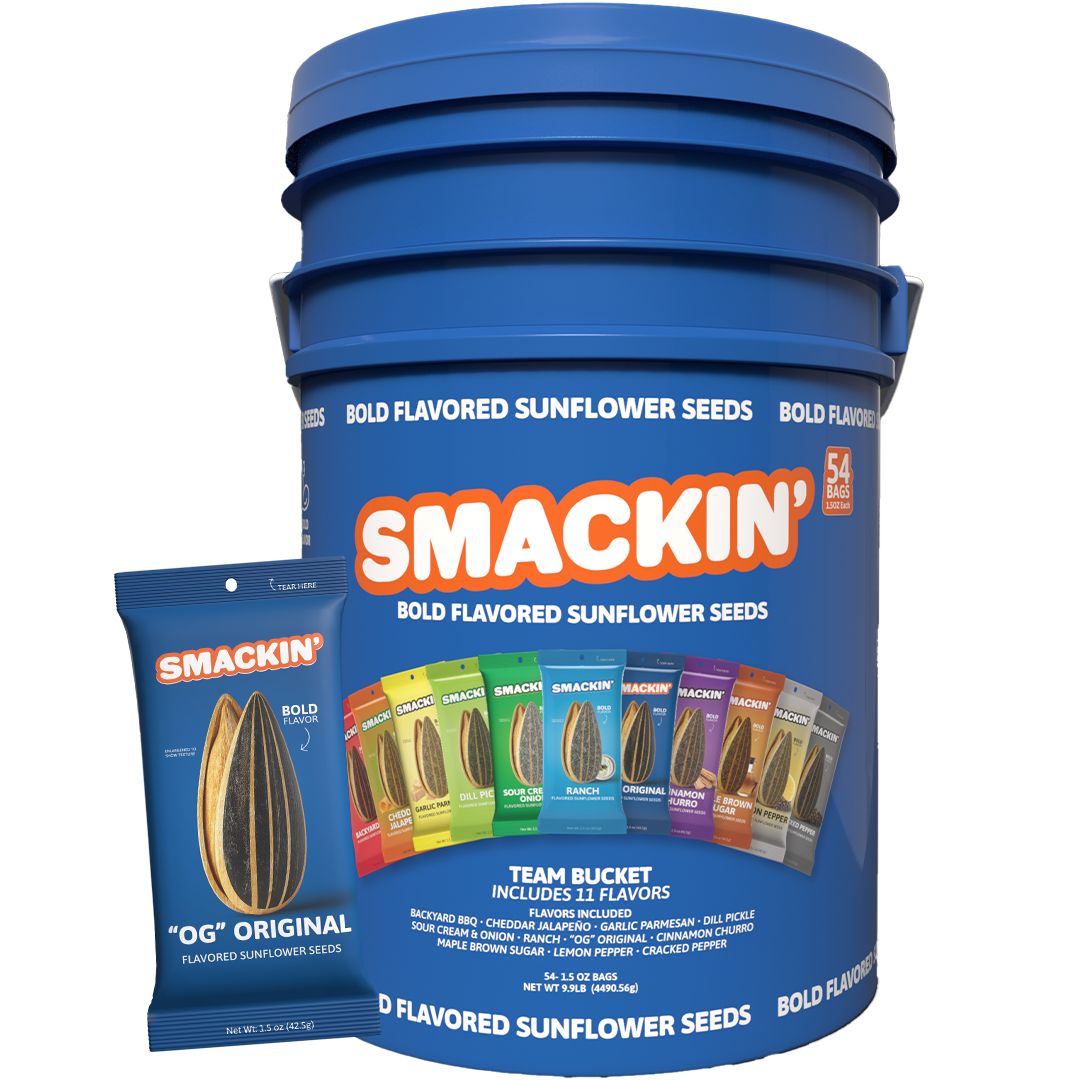 Product photography of a large royal blue Smakin Bold Flavored Sunflower Seeds Team Bucket containing 54 bags and showcasing 11 colorful flavor pouches including Backyard BBQ, Dill Pickle, and Ranch, with a smaller blue OG Original bag standing beside it