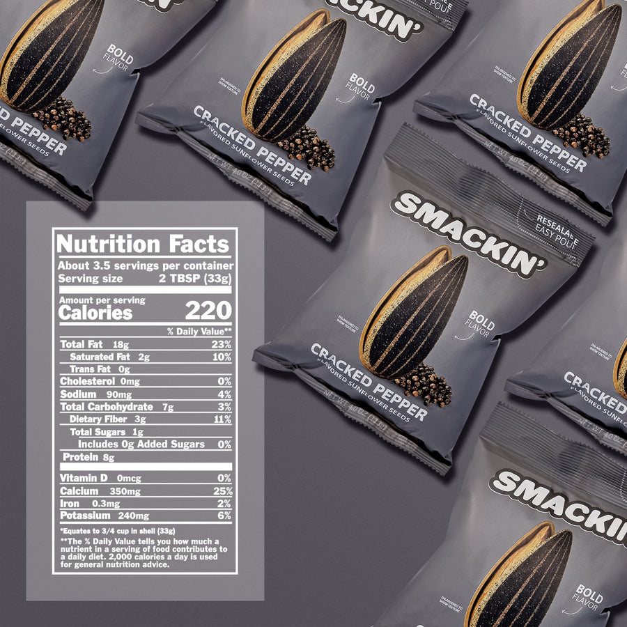 Product photograph of multiple dark grey Smackin' Cracked Pepper Flavored Sunflower Seeds bags on a grey surface, each bag featuring a striking graphic of an enlarged sunflower seed and black peppercorns, "Bold Flavor" text, and a visible white Nutrition Facts label on the bottom left detailing 220 calories