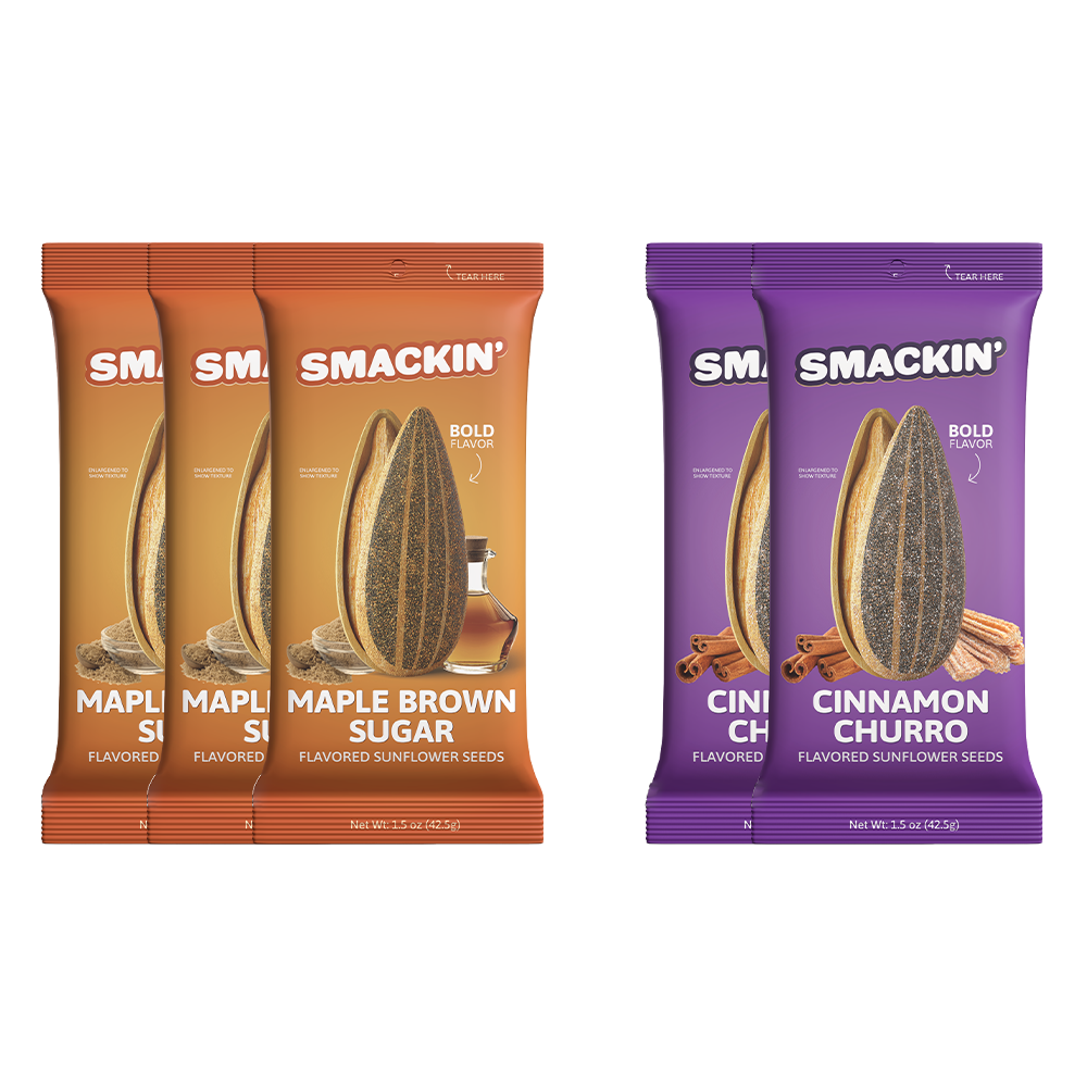 Studio shot of three orange Smackin' Maple Brown Sugar flavored sunflower seed pouches depicted with maple syrup alongside two purple Smackin' Cinnamon Churro flavored sunflower seed pouches shown with churros and cinnamon sticks, all featuring a large sunflower seed illustration and 'Bold Flavor' text